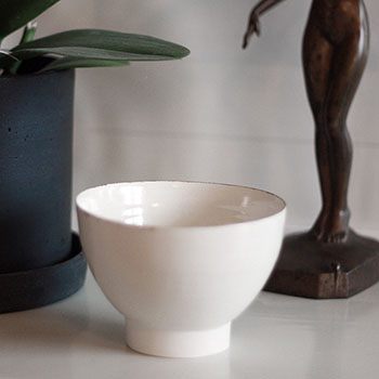 White porcelain bowl with a thick foot and a thin golden rim on a white surface